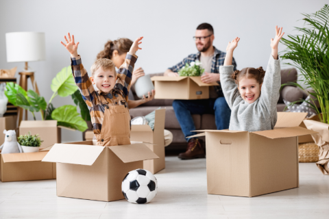 Two children sitting in cardboard boxes with their hands in the air.  