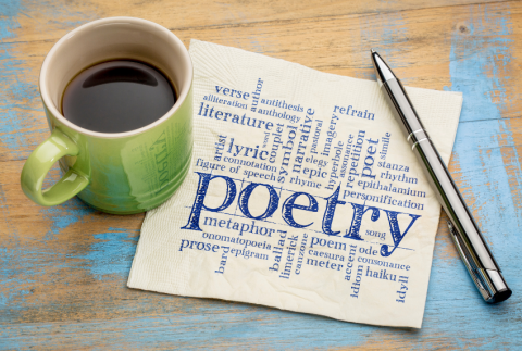 Napkin with poetry words on it, cup of coffee on one side and a pen on the other.