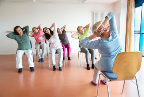 Ladies sitting on chairs leaning towards one side with arms behind their heads.