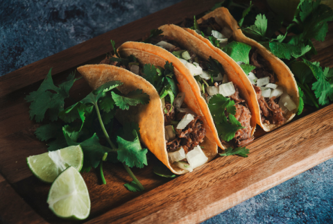 Tacos lined up on a board. 