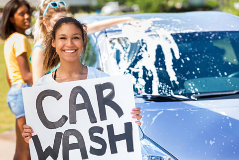 Girl holding sign that reads car wash. 