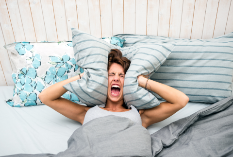 Lady in bed screaming with pillow by ears. 