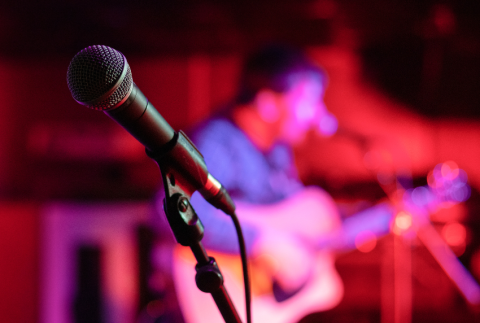 Microphone with person in back holding a guitar. 