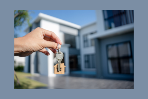 Hand holding keys in front of a house.