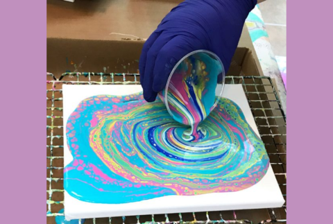 Top view of hand pouring paint onto a canvas. 