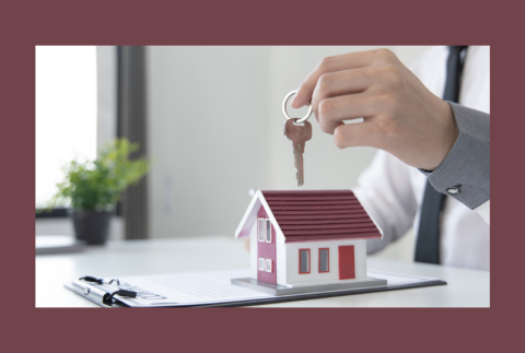 Toy home with a person holding a key over it. 