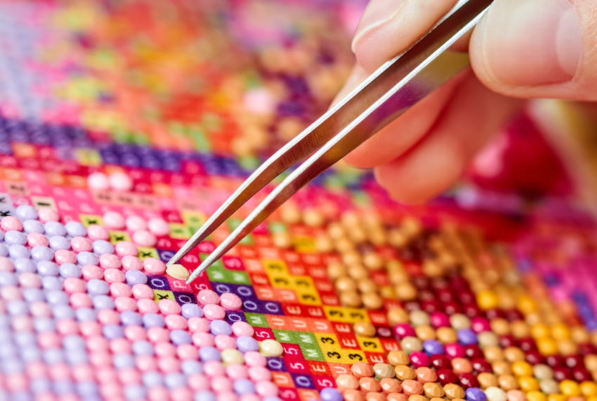 Hand with tweezers placing diamonds on painting.