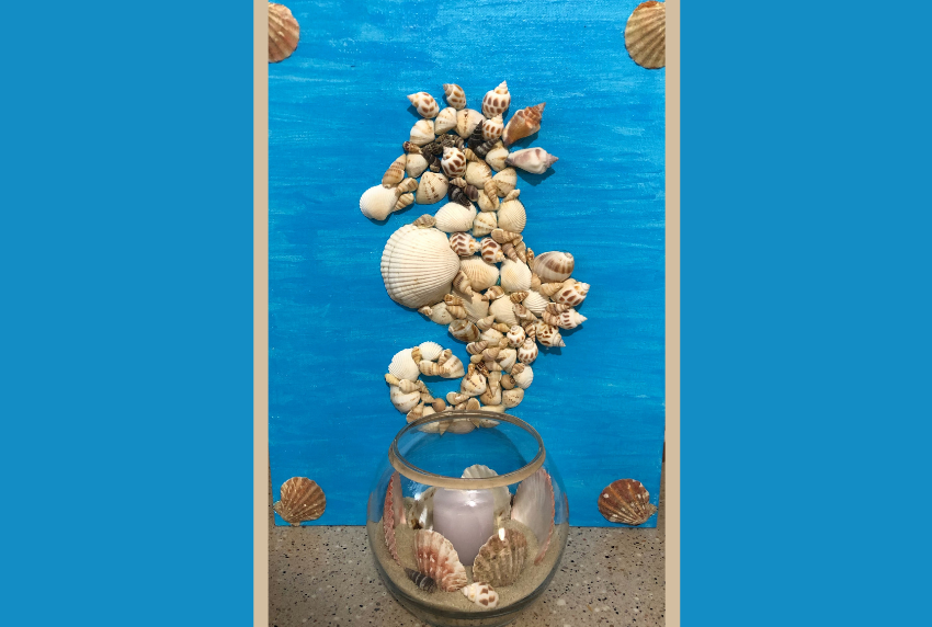 Craft of a seahorse made out of seashells with a bowl filled with sand in front of it.