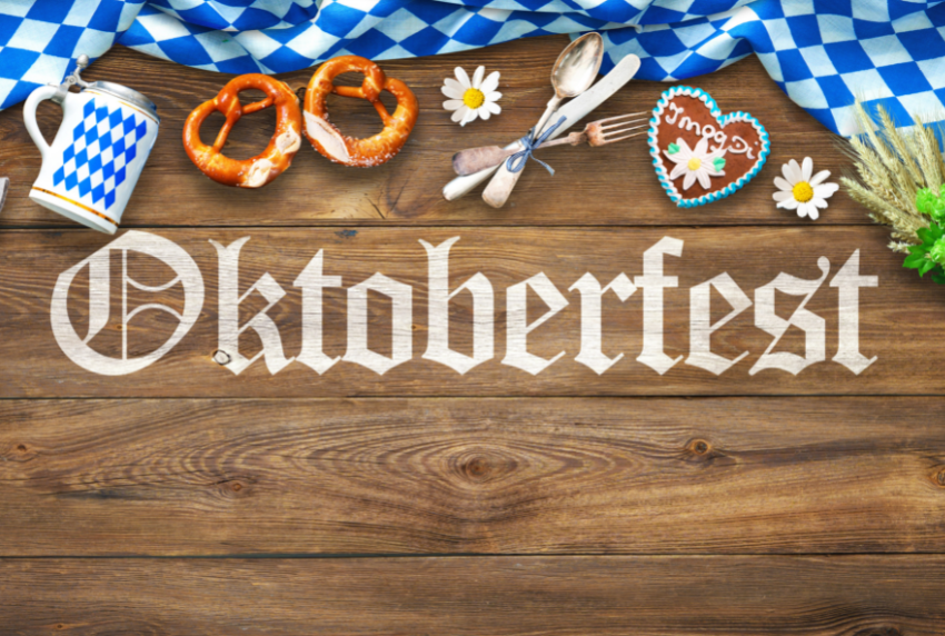 Word Oktoberfest written on a board surrounded by pretzels and cutlery. 