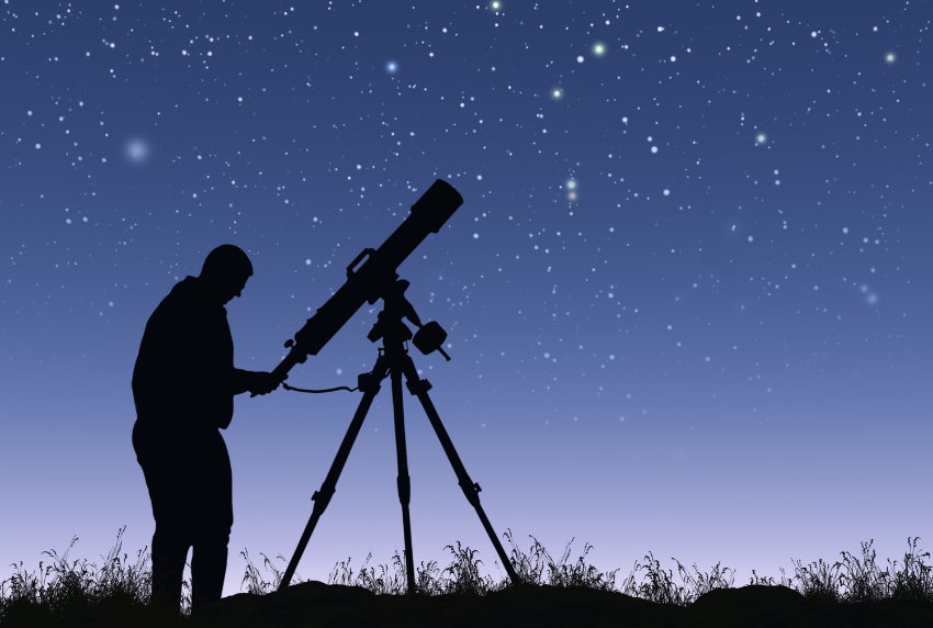 Silhouette of a man stargazing with a telescope.