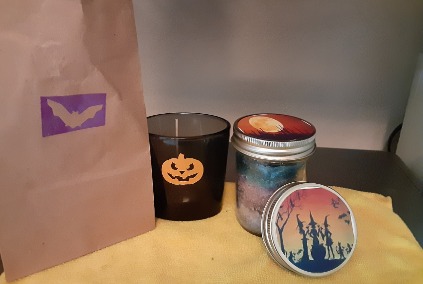 Brown paper bag with a bat, black candle jar with a pumpkin and one with witches. 