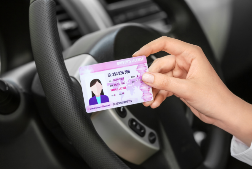 Hand holding license in front of a steering wheel.