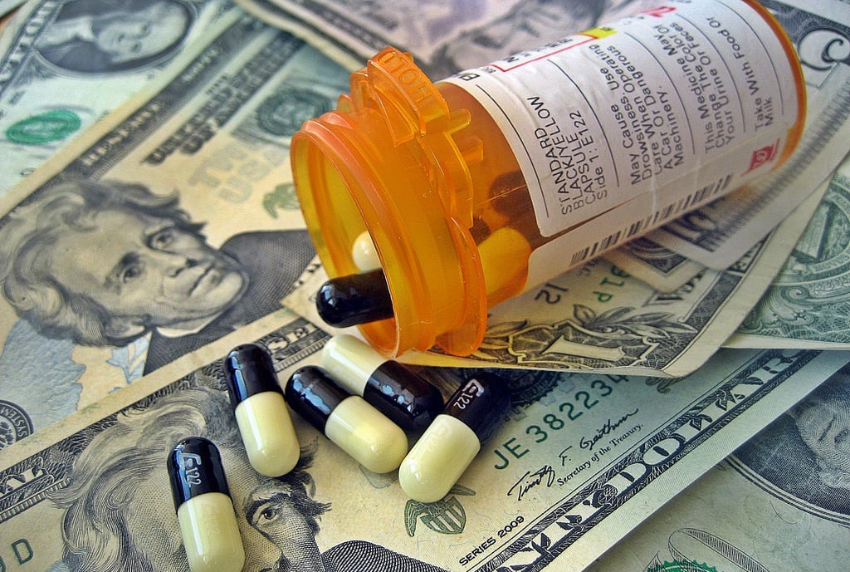 Picture of a prescription bottle with pills spilling out on top of 20 dollar bills