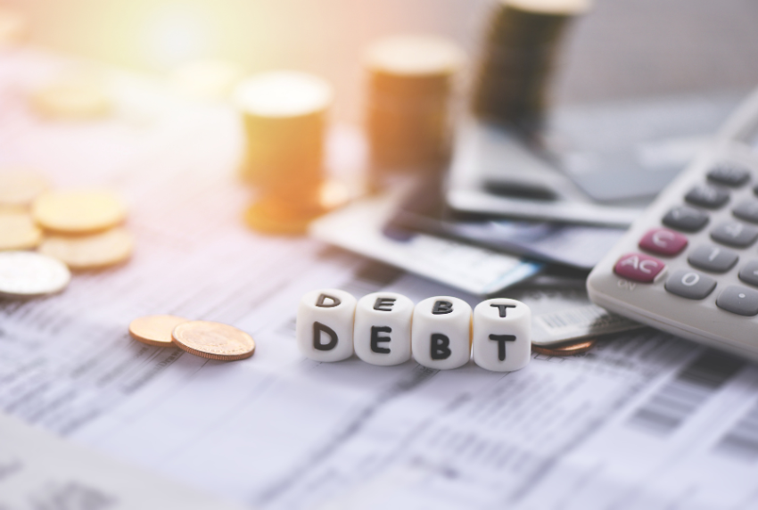 Calculator, stack of coins and the word debt. 