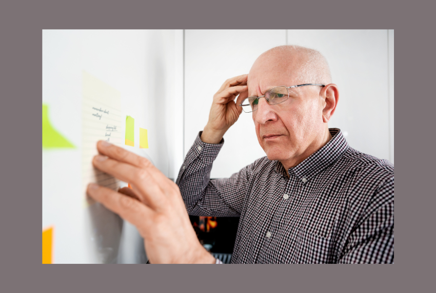 Man holding head with one hand and other hand on words on a board. 