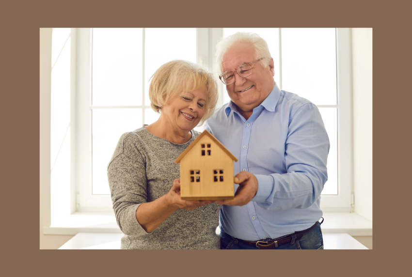 Elderly couple holding a wooden shaped house. 